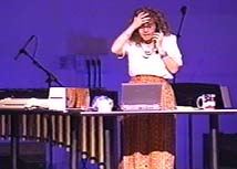 A woman holding her head while talking on a phone at her cluttered desk.