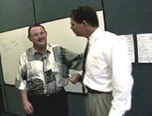 A man talks with another man in a white shirt and tie.