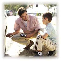 A man teaching his son how to check the air pressure in a car tire.